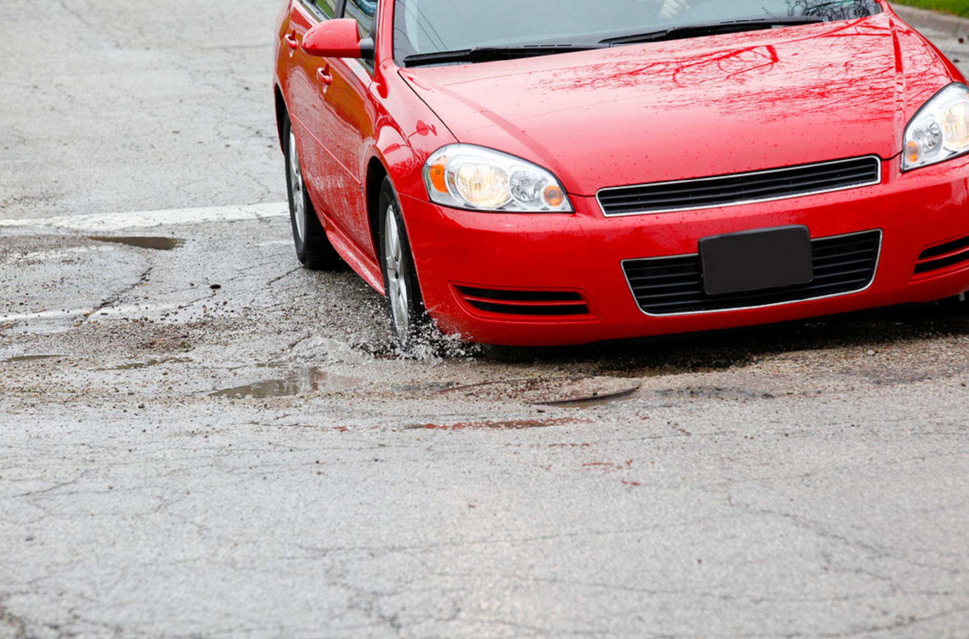 Red sedan passenger car driving over a pothole in the city